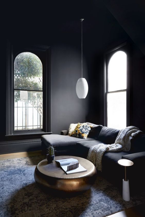 a moody living room with soot walls and a matching sectional, a metal coffee table and a white pendant lamp