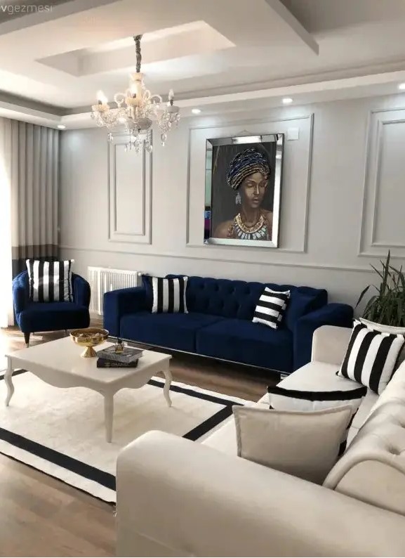 a neutral living room with a navy sofa and chair, a creamy sofa, a vintage coffee table and striped pillows and a rug plus a chic crystal chandelier