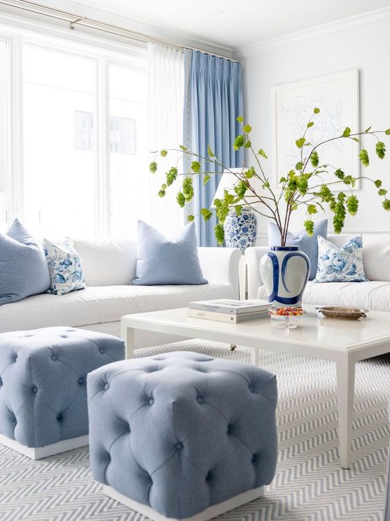 a pretty living room with white seating furniture, blue poufs and pillows, a low coffee table and blue curtains