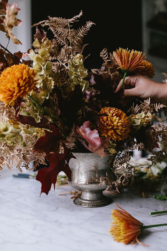 a refined Halloween centerpiece of orange chrysanthemums, dark leaves, greenery and a silver goblet is amazing