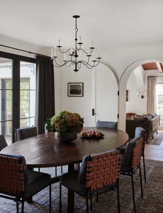 a refined dining room with an oval dark-stained table, black woven chairs, potted greenery and a vintage chandelier
