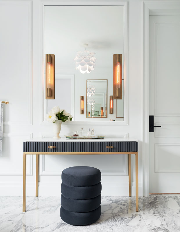 a refined entryway with a large mirror, a soot vanity with a ribbed surface, a soot pouf and chic sconces