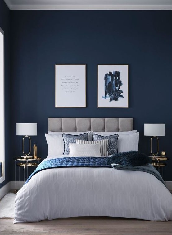 a-refined-modern-bedroom-with-navy-walls-a-grey-upholstered-bed-chic-artworks-gold-nightstands-and-blue-bedding.jpg