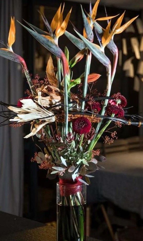 a scary Halloween floral arrangement with orange and burgundy blooms and greenery plus corn cobs