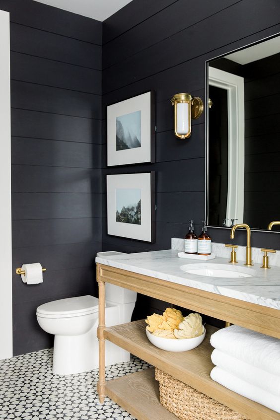 a soot bathroom with a light-stained vanity abd baskets, a mirror, sconces and a mini gallery wall is cool