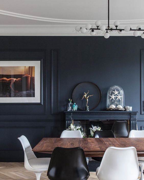 a soot dining room with a fireplace, a stained dining table, black and white chairs, an artwork and some decor