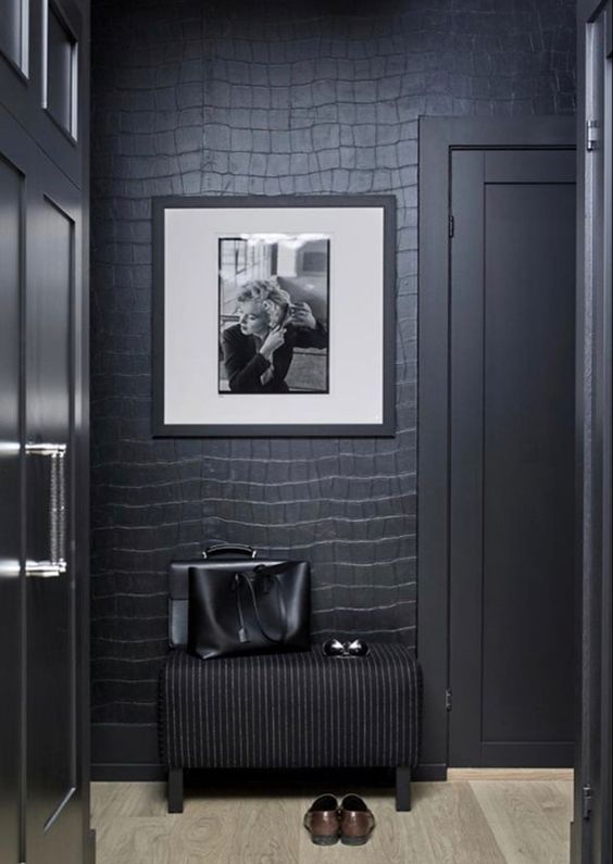 a soot entryway with reptile print wallpaper, a black pouf, an artwork and some cabinetry is very chic and refined
