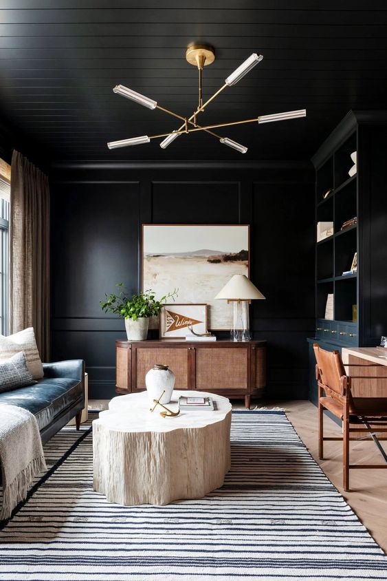 a soot home office with a black leather sofa, a stained credenza, a desk and a chair, a chandelier, a bleached stump table