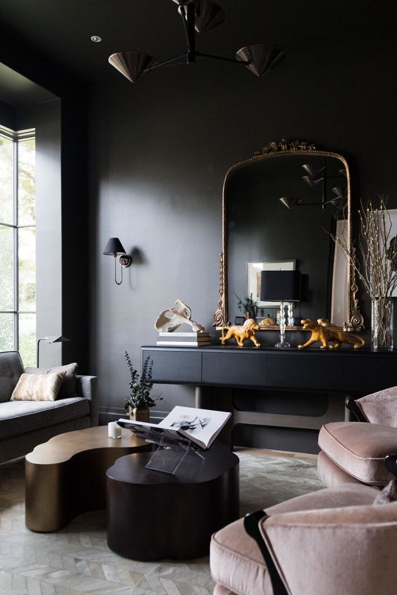 a soot living room with a black console and a chic mirror, blush chairs, a grey sofa, eye-catching coffee tables