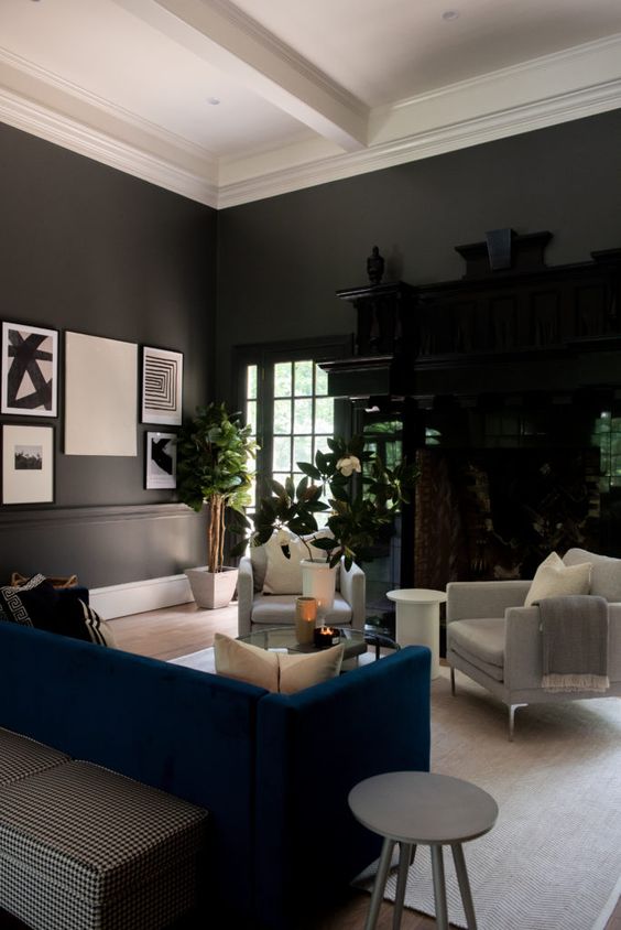 a soot living room with a dark-stained storage unit, creamy chairs, a navy sofa, a glass coffee table and potted plants