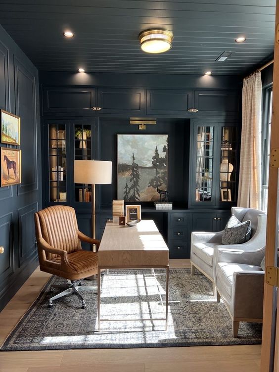 a soot modern farmhouse home office with a soot ceiling, walls and built-inc abinets, a light-stained desk, an amber chair and creamy ones
