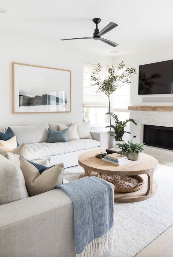 a soothing living room with a built-in fireplace, neutral sofas, blue and white pillows, a wooden coffee table and greenery