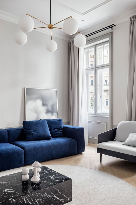 a sophisticated contemporary living room with a blue sofa, a white chair, a black marble coffee table and a statement chandelier