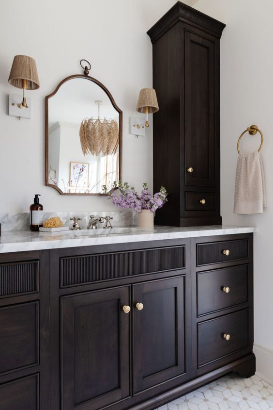 a sophisticated dark-stained vanity with gold knobs, a vintage mirror and sconces create a very elegant and somewhat dramatic look