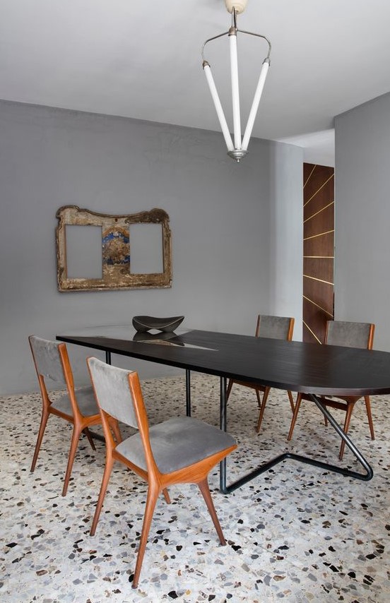 a sophisticated dining room with grey walls and black, grey and white terrazzo, a dark-stained table and grey chairs plus a unique chandelier