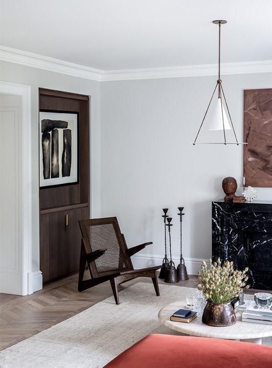 a sophisticated living room with a fireplace clad with black stone, a dark-stained storage unit and a matching chair, a coffee table and a pendant lamp