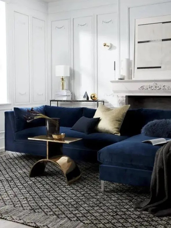 a sophisticated living room with paneling, a vintage fireplace, a midnight blue sofa, navy and gold pillows, a gold side table and some table lamps