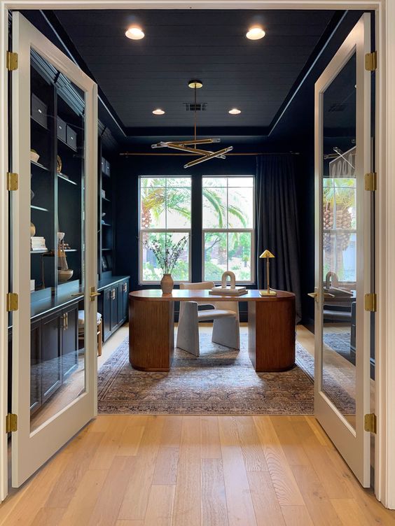 a sophisticated soot home office with built-in cabinets, a stained desk, a creamy chair and a gold chandelier