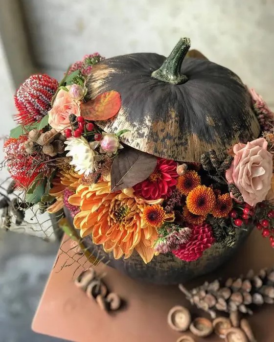 a stunning black and gold Halloween pumpkin with orange, red, blush and black blooms, berries and pincushion proteas