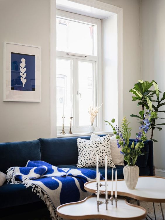a stylish Scandinavian living room with a navy sofa, printed pillows, side tables, a blue and white art and greenery
