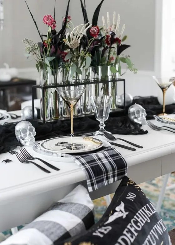 a stylish blackm white and silver Halloween tablescape with a black runner, plaid napkins, silver skulls, spiders and bold blooms