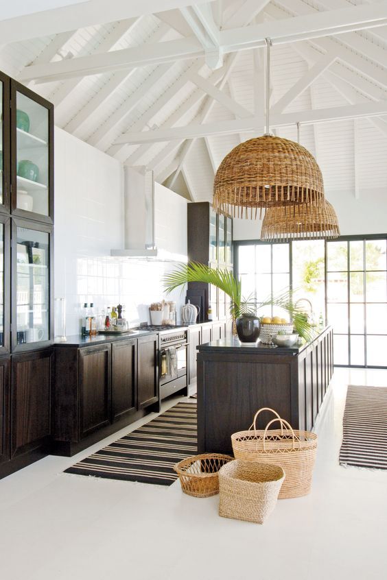 a stylish kitchen with dark-stained cabinets and a large kitchen island, woven pendant lamps and greenery is amazing