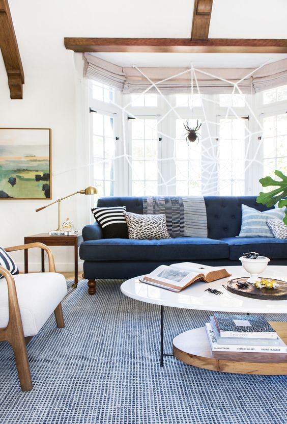 a stylish living room with a navy sofa, white chairs, a tiered coffee table, a blue rug and some plants is very chic