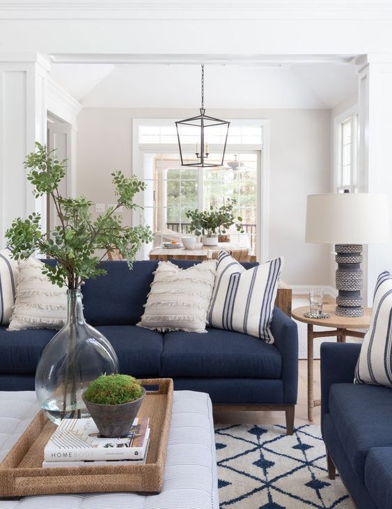 a stylish living room with navy sofas and printed pillows, a printed rug, an ottoman, some greenery is very welcoming