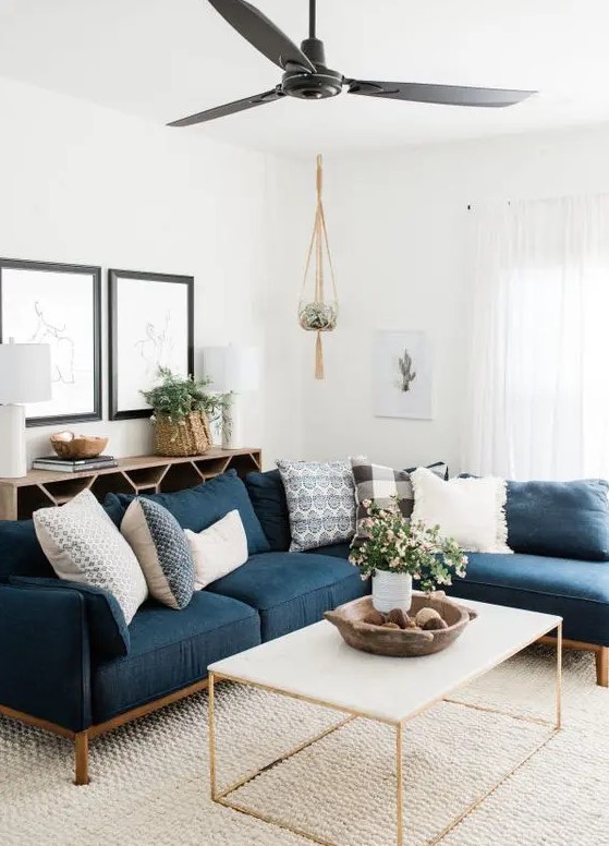 a stylish mid-century modern neutral living room with a navy sectional, a coffee table, a lovely credenza, some pretty artwork and potted greenery and blooms
