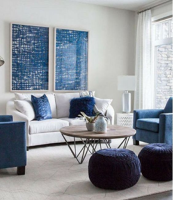 a stylish modern living room with a white sofa and blue pillows, blue chairs, midnight blue poufs, blue artwork and a coffee table