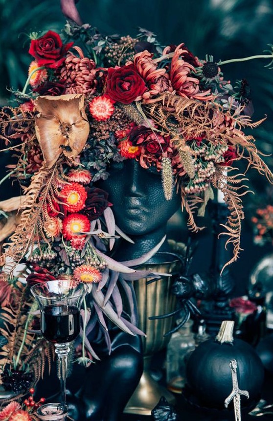 a unique and lush Halloween centerpiece of a black human bust, dried leaves and greenery plus pink and red blooms