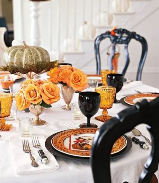 an elegant Halloween tablescape with orange and black plates and glasses, orange roses in gold vases and a metallic pumpkin on a stand