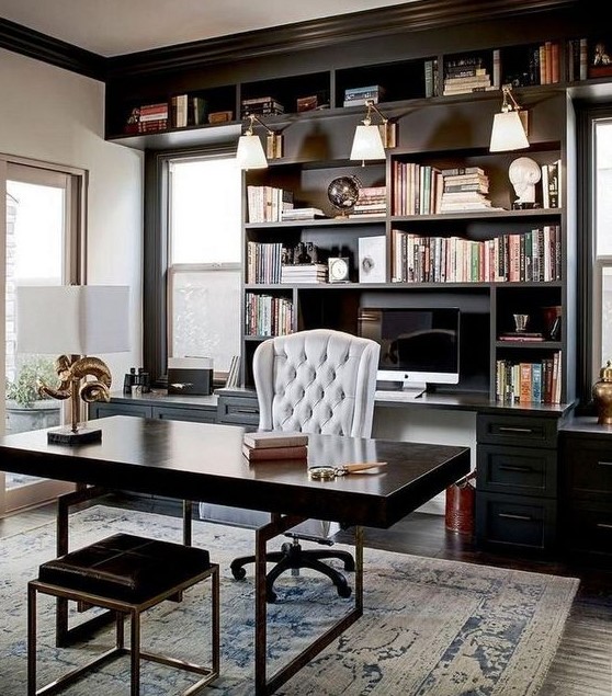 an elegant and chic masculine home office with a wooden desk and a stool, a built-in bookcase and much natural ligjt