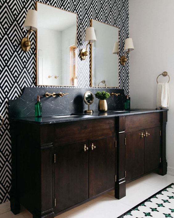 an elegant bathroom with a geo print wall, a double dark-stained vanity with a black stone countertop and elegant sconces