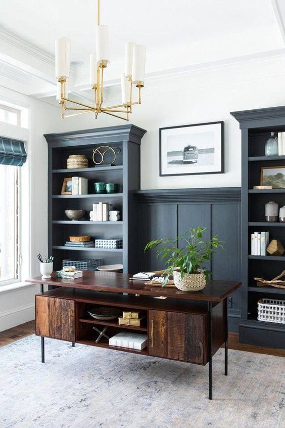 an elegant home office with graphite grey built-in shelves, a dark-stained desk and some decor plus a chic chandelier