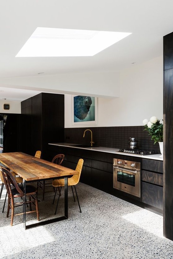 an elegant kitchen with a black and white terrazzo floor, dark stained cabinets, a stained table and woven chairs is lovely