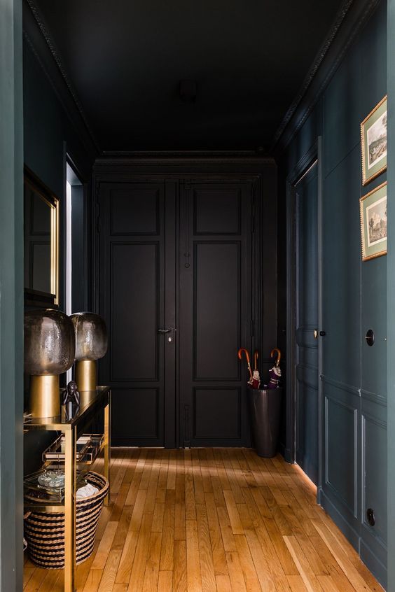 an elegant soot entryway with a gold console table, table lamps, a basket, a bucket with umbrellas and artwork