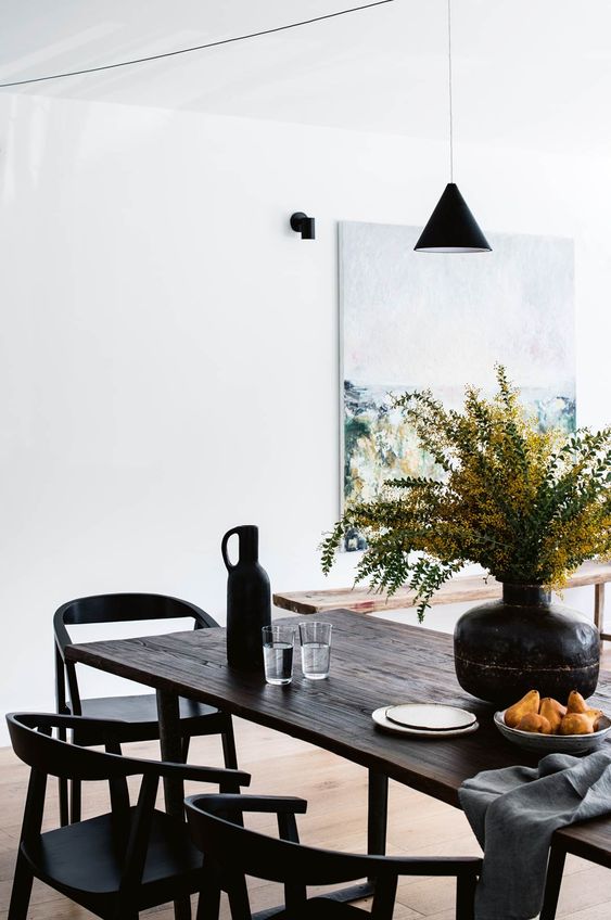 an exquisite modern dining space with a dark-stained reclaimed table and black chairs, a pendant lamp and some blooms