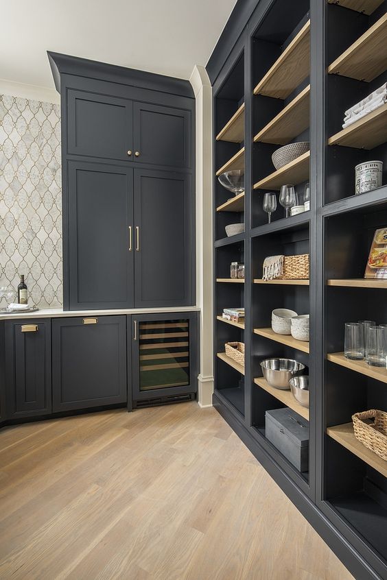 an exquisite soot pantry with built-in cabinets and shelves, gold handles and baskets plus a tiled wall is a lovely and cool space