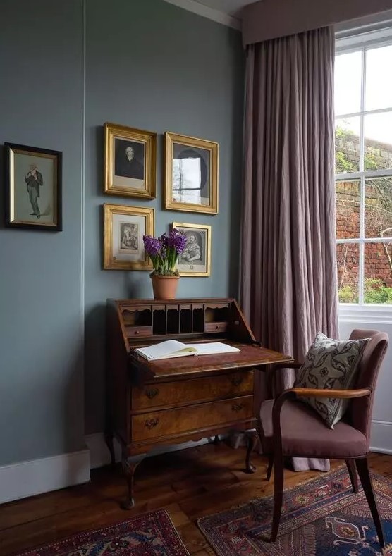 an exquisite vintage working nook with grey walls, a vintage dark-stained bureau and a mauve chair, mauve curtains and a gallery wall