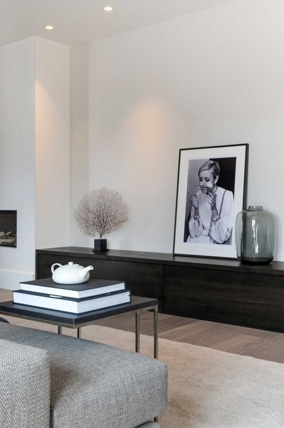 an ultra-minimal living room with a dark stained storage unit, a grey sofa, a black table and a statement artwork