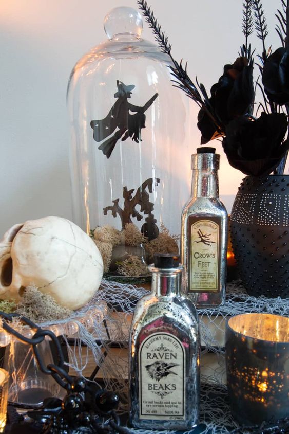 catchy Halloween decor with vintage posion bottles, skulls, candleholders, a cloche with a witch scene and a black vase with black blooms