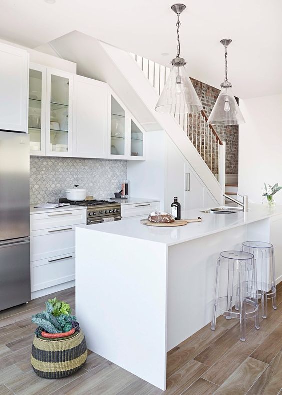 a beautiful built-in kitchen integrated into the stairs, with a kitchen island and clear acrylic stools, pendant lamps