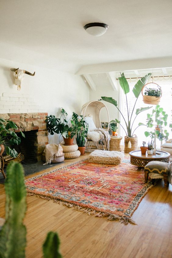 a bright boho living room with a fireplace, a bold rug, a chair, potted plants, a coffee tale and some cathcy decor