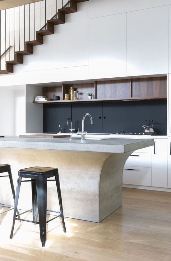 a refined contemporary kitchen with sleek cabinets built in under the stairs, with a black backsplash, a catchy kitchen island