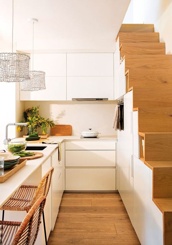 a small modern white kitchen partly built into the staircase, with a kitchen island that doubles as a dining zone