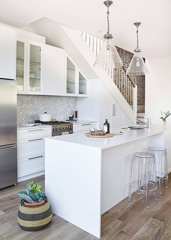 a white modern farmhouse kitchen placed under the stairs with cabinets built in, a scallop tile backsplash, a kitchen island