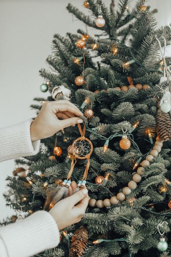a boho Christmas tree with wooden beads, white tassels, lights, blooms and dream catcher ornaments plus boho pillows under it