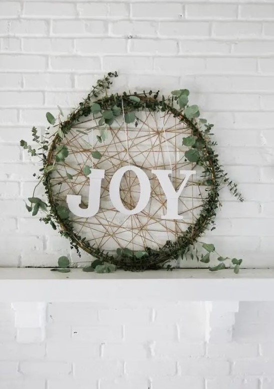 a creative modern Christmas wreath of an embroidery hoop, covered with eucalyptus, yarn and with letters looks awesome