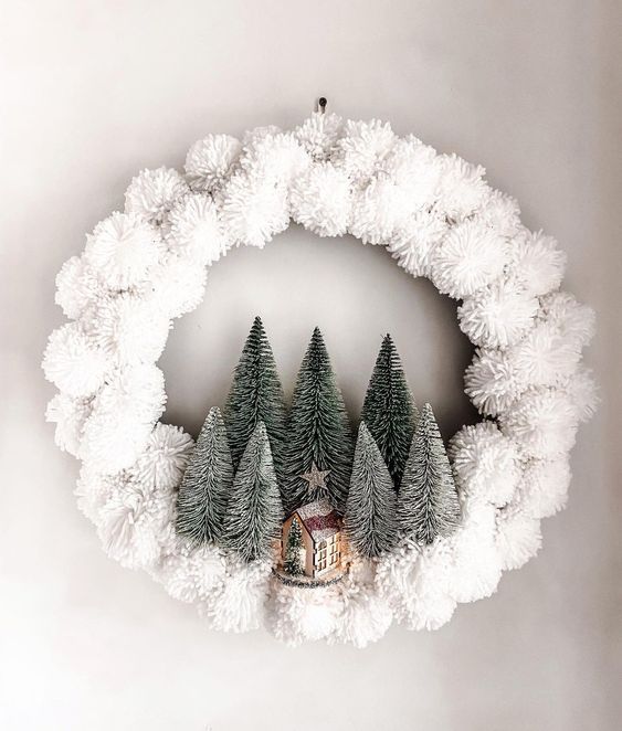a cute modern Christmas wreath of white pompoms, bottle brush Christmas trees and a small house is a lovely solution